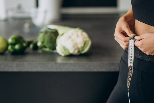 Young woman with measuting tape on weist at the kitchen